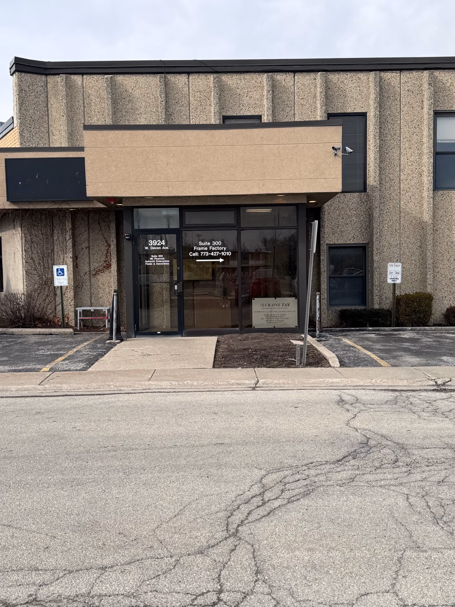 Front exterior of a beige building with glass entrance and parking spaces.