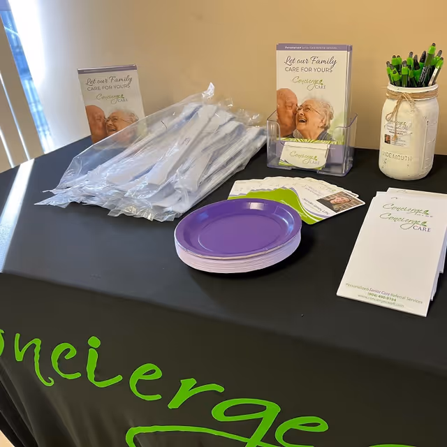 Table displays Concierge Care branding materials, brochures, plates, pens, and a jar on a black table.