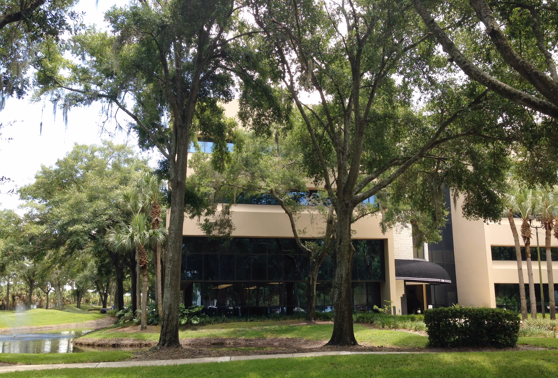 Front exterior view of a senior living facility with trees, glass windows, and an entrance canopy.