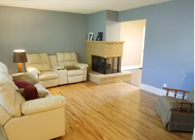 A cozy living room with beige leather sofas, a brick fireplace, and blue walls.