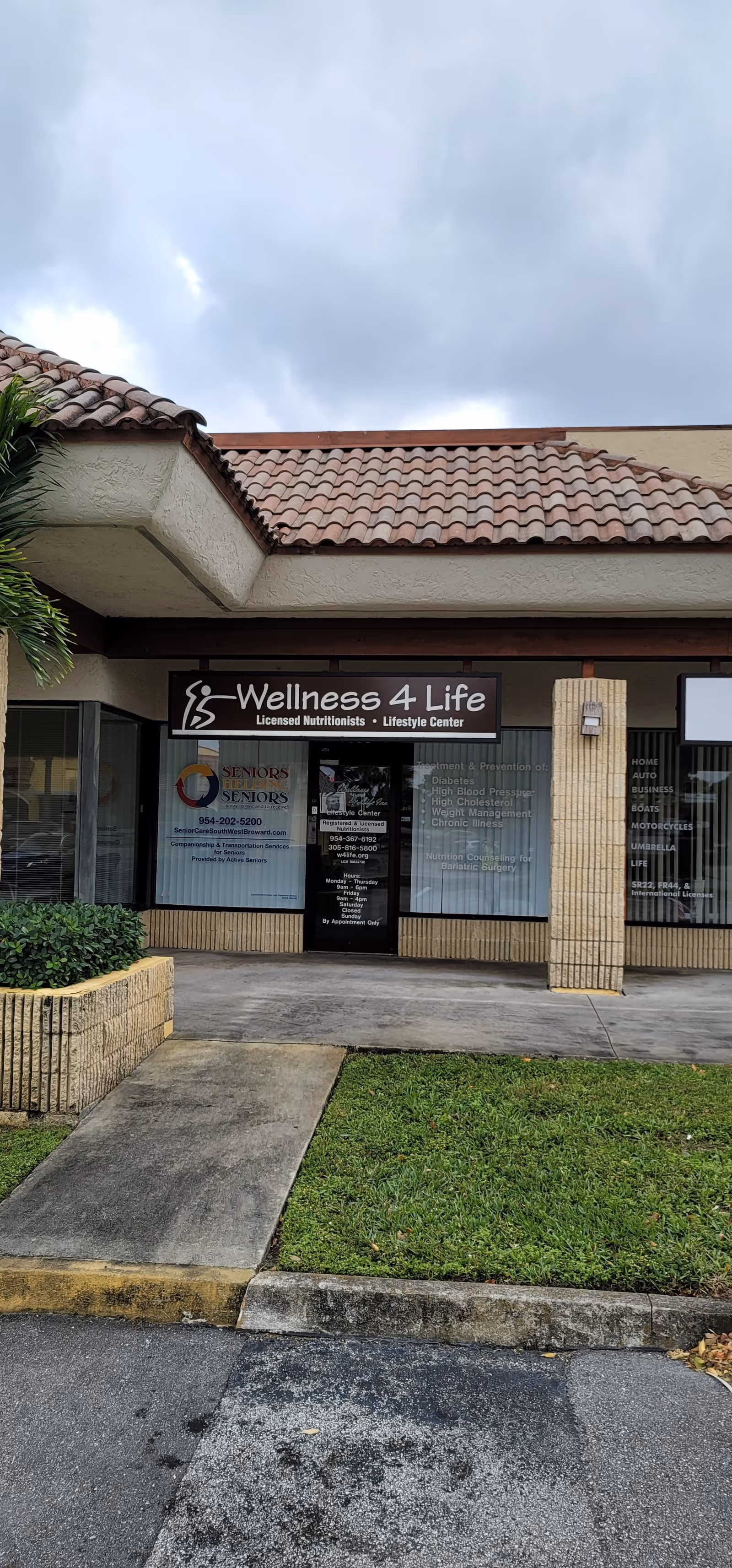Storefront with Wellness 4 Life sign, glass windows, sidewalk, and cloudy sky.