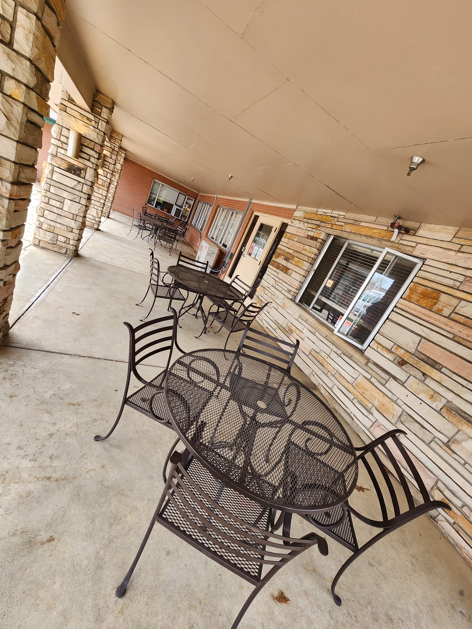 Outdoor patio with metal tables and chairs along a stone-walled building at Prestige Care Center.