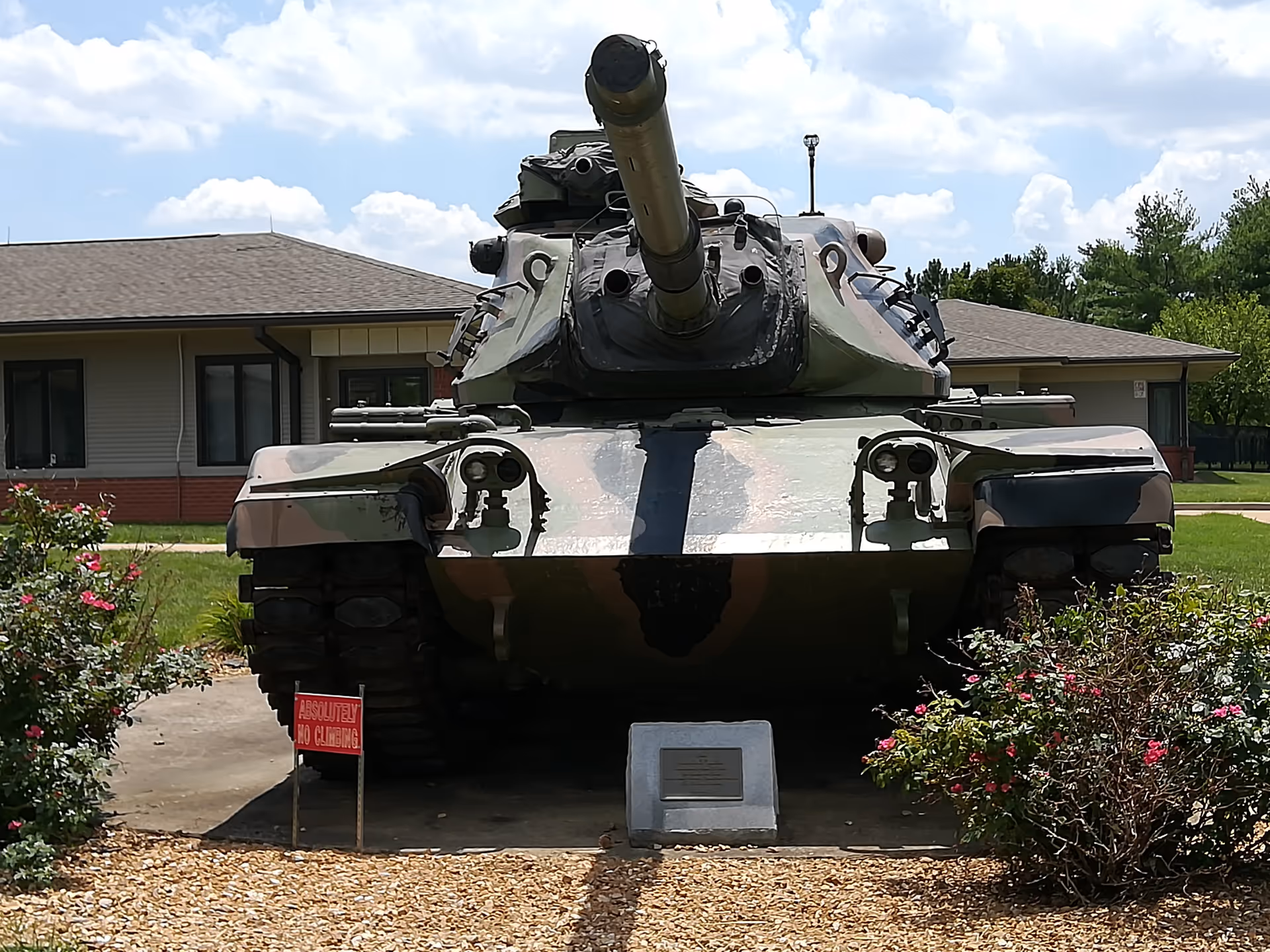 A military tank on display in front of a single-story facility with landscaping.