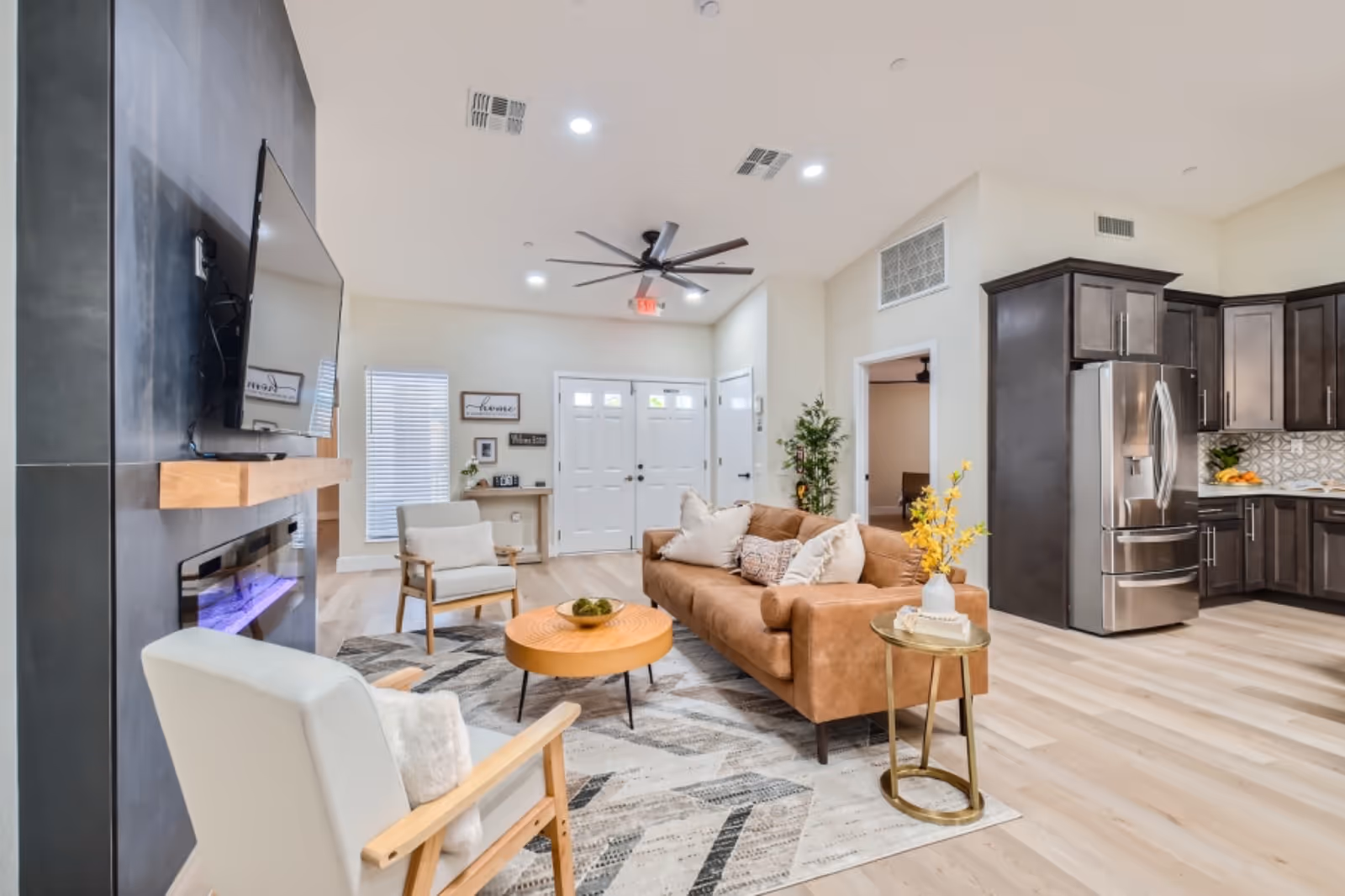 Open-concept living room in a senior facility with sofa, chairs, TV, and nearby kitchen.