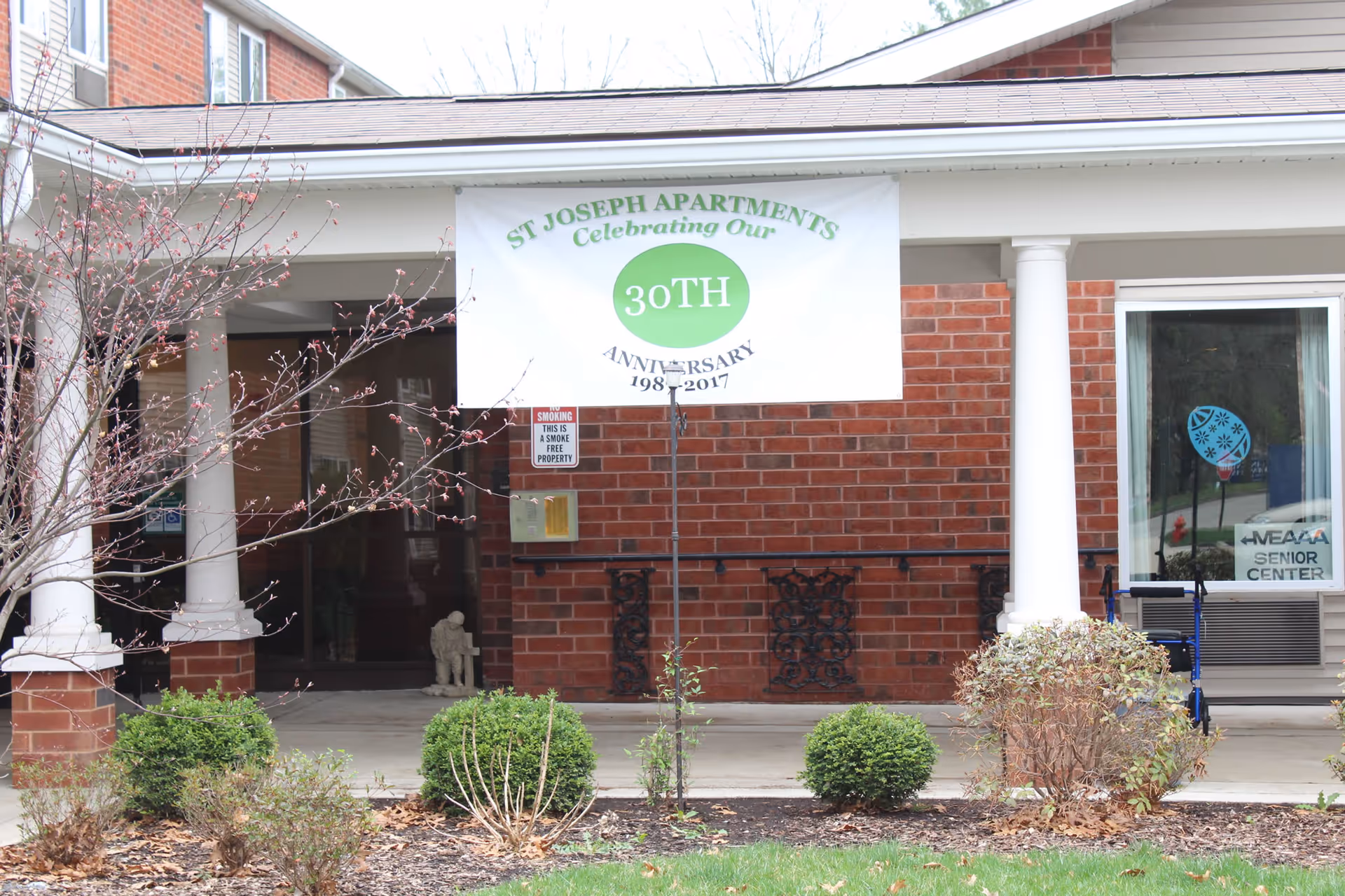 Front entrance of St Joseph Apartments with brick facade, white columns, and a banner.