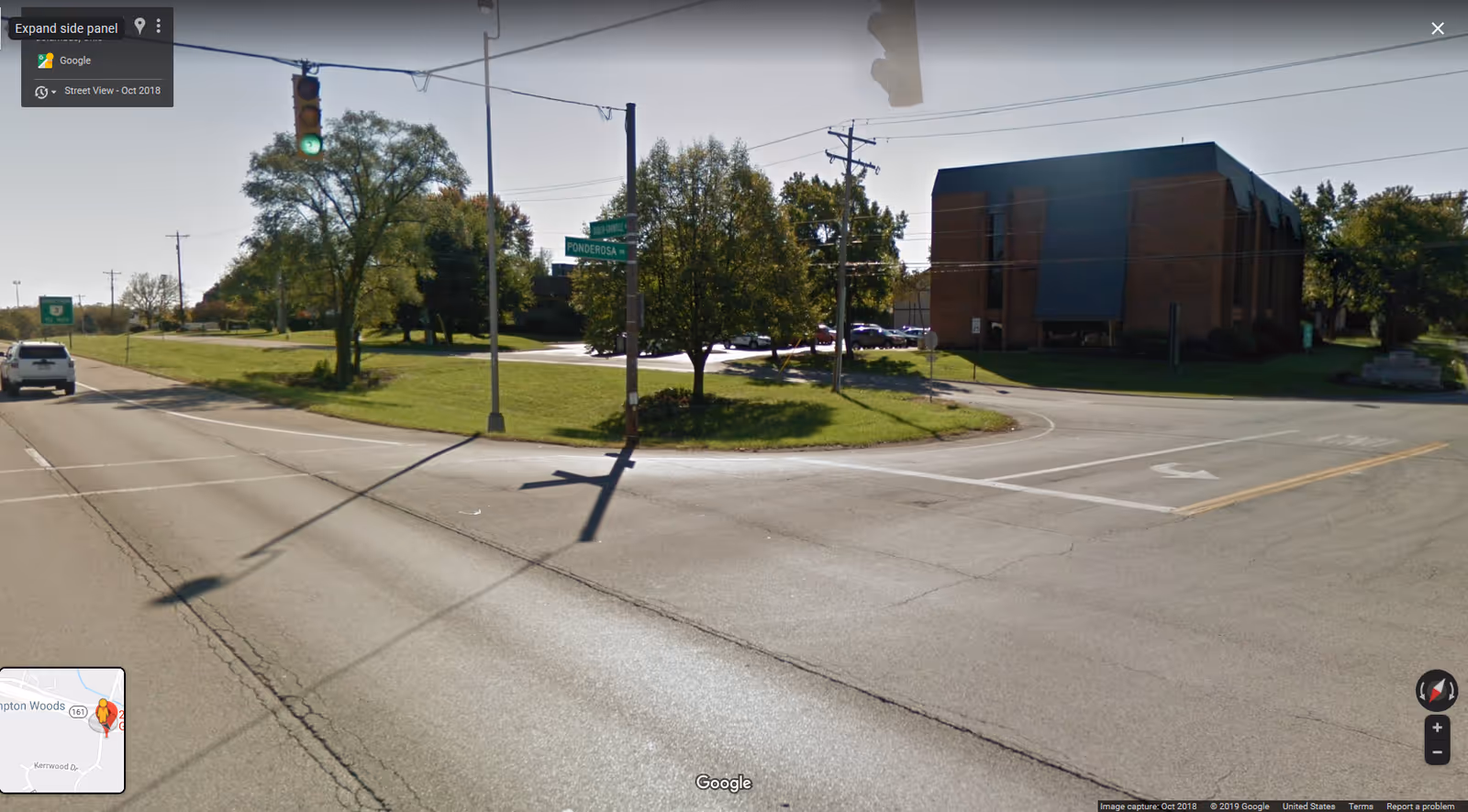 Wide street intersection with a brick building and green trees on a sunny day.