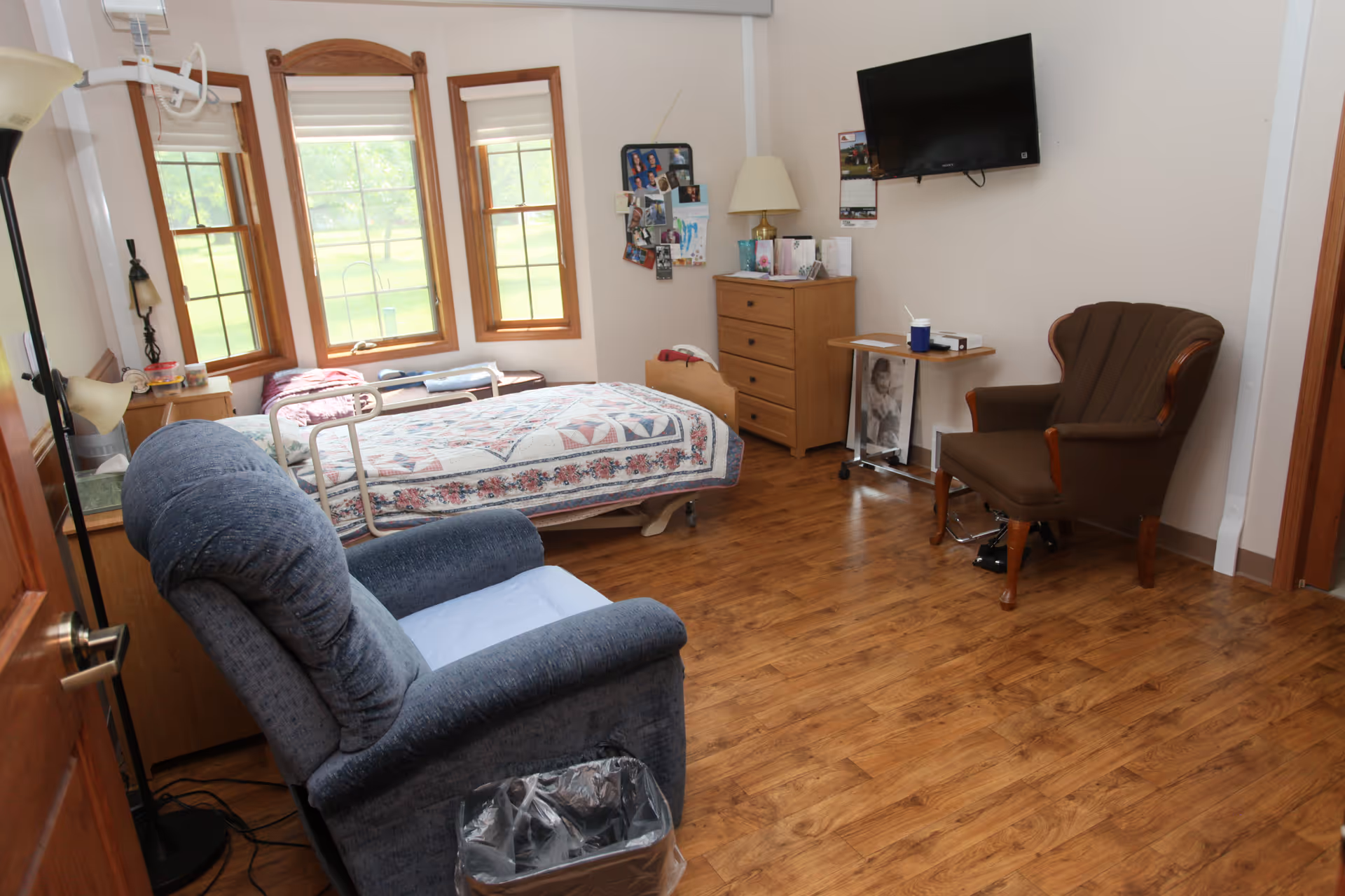 A furnished bedroom with a bed, recliner, dresser, and wall-mounted TV.