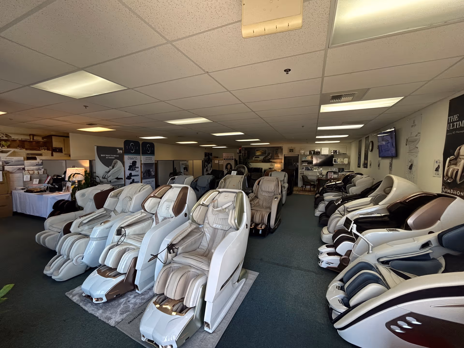Row of massage chairs in a spacious showroom with displays and banners.