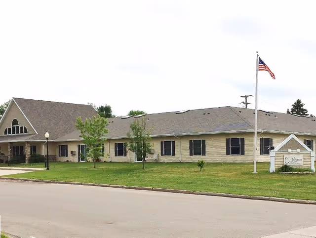 Front view of a single-story beige Good Samaritan Society Lakota facility with lawn and flagpole.