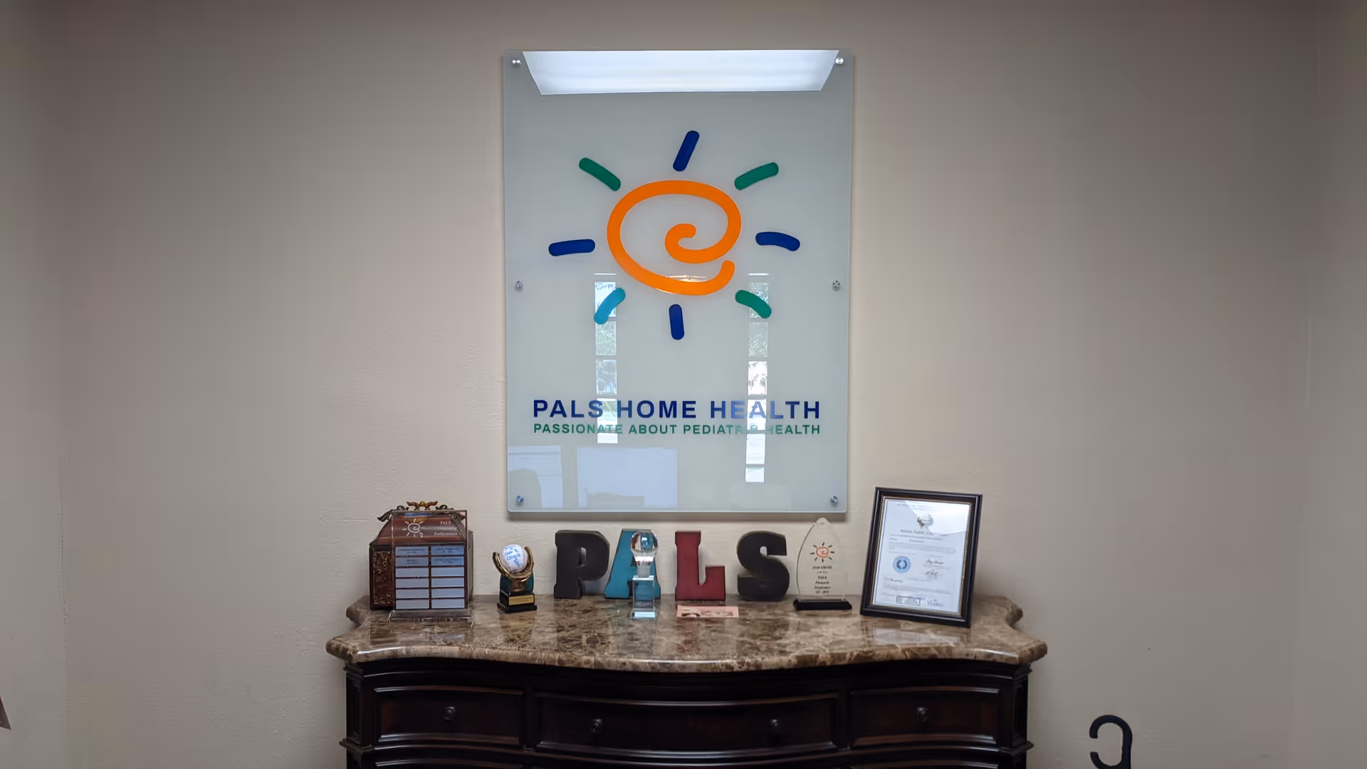 Reception desk in a lobby with PALS Home Health sign on glass behind.
