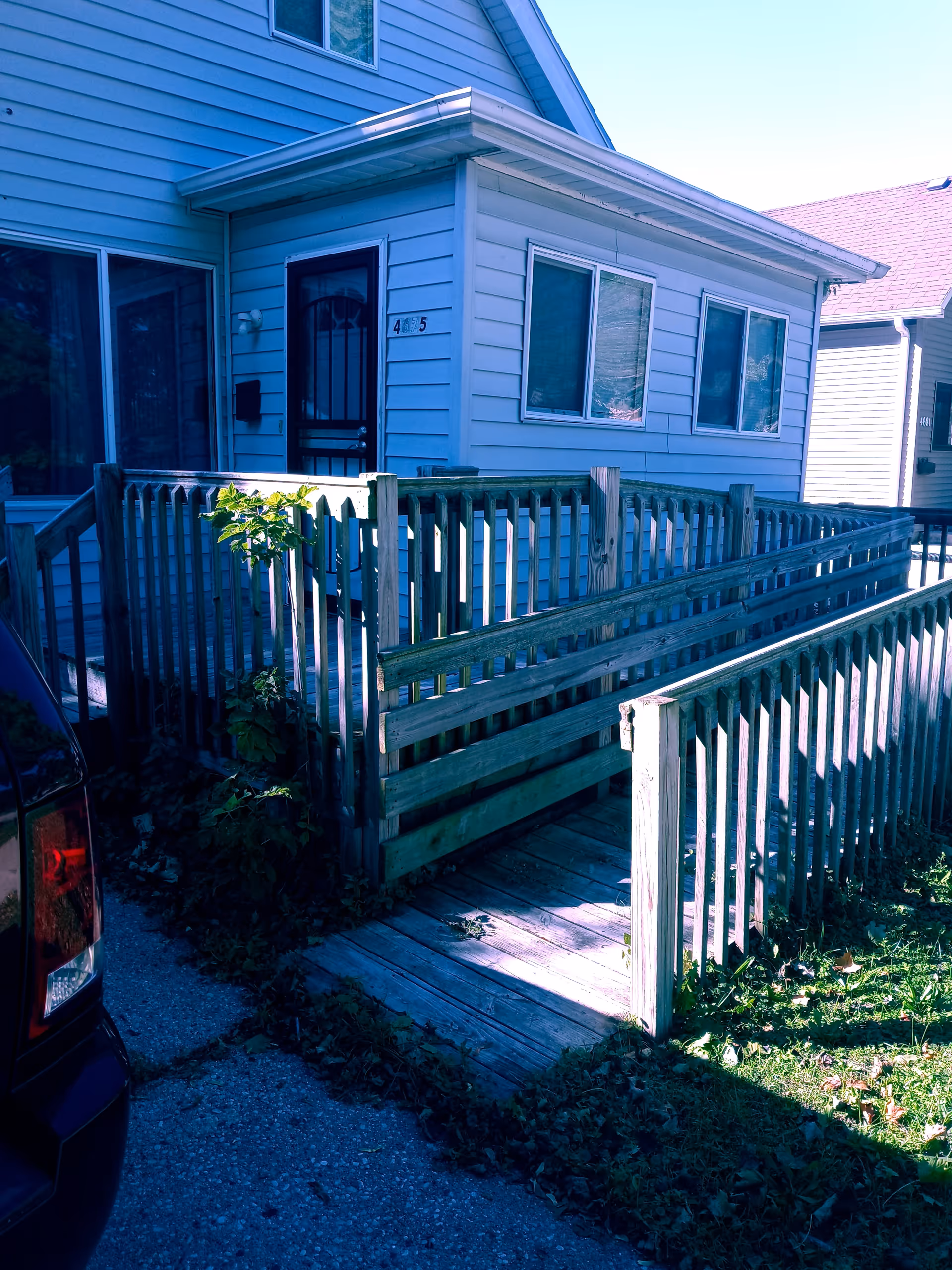 Blue facility exterior with a wooden ramp and railing leading to a front door.