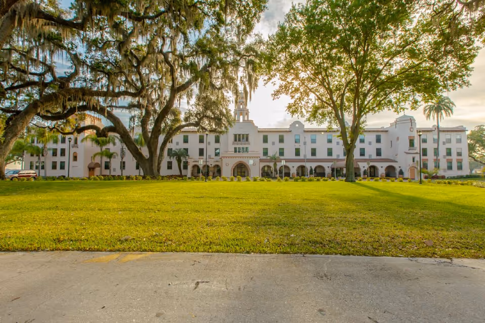 White multi-story senior living building with arches, trees, and a manicured green lawn.