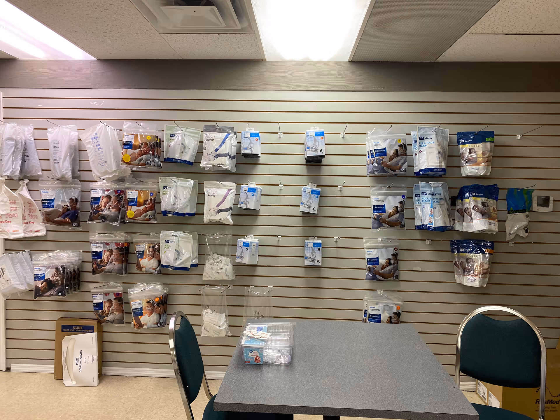 Wall of packaged medical supplies on a slatwall with a table.