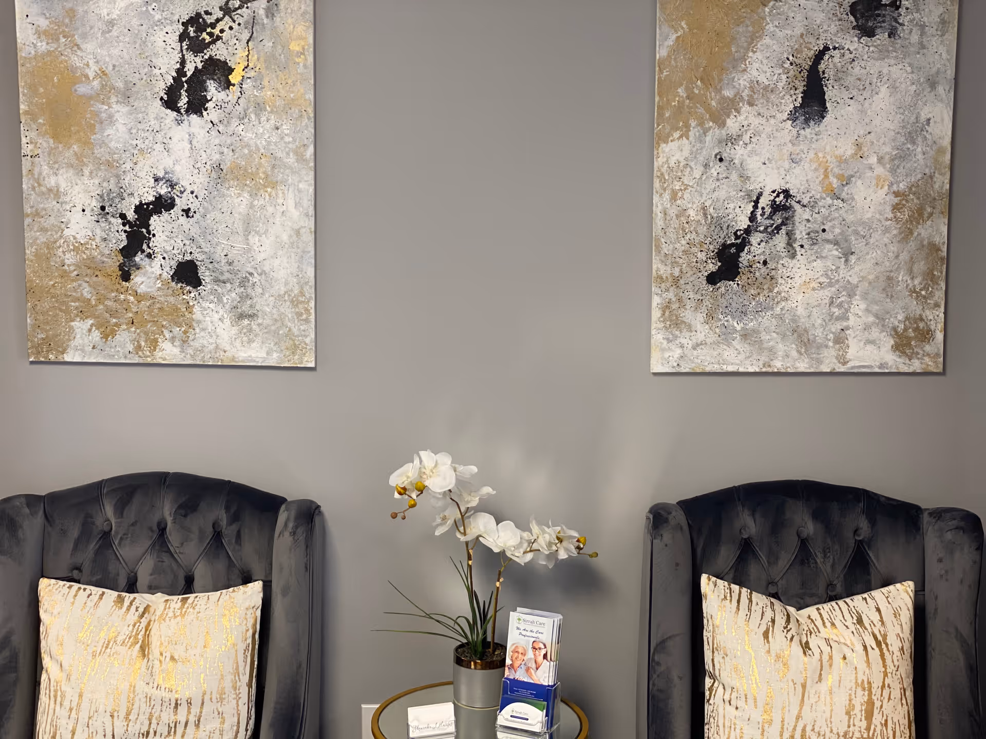 Two tufted chairs frame a round table with an orchid and wall art.