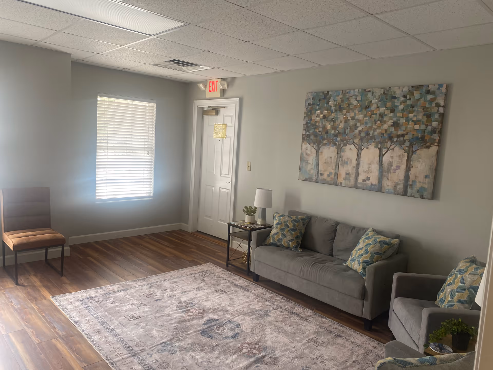 Bright lounge area in a senior living facility with sofa, chairs, rug, and wall art.