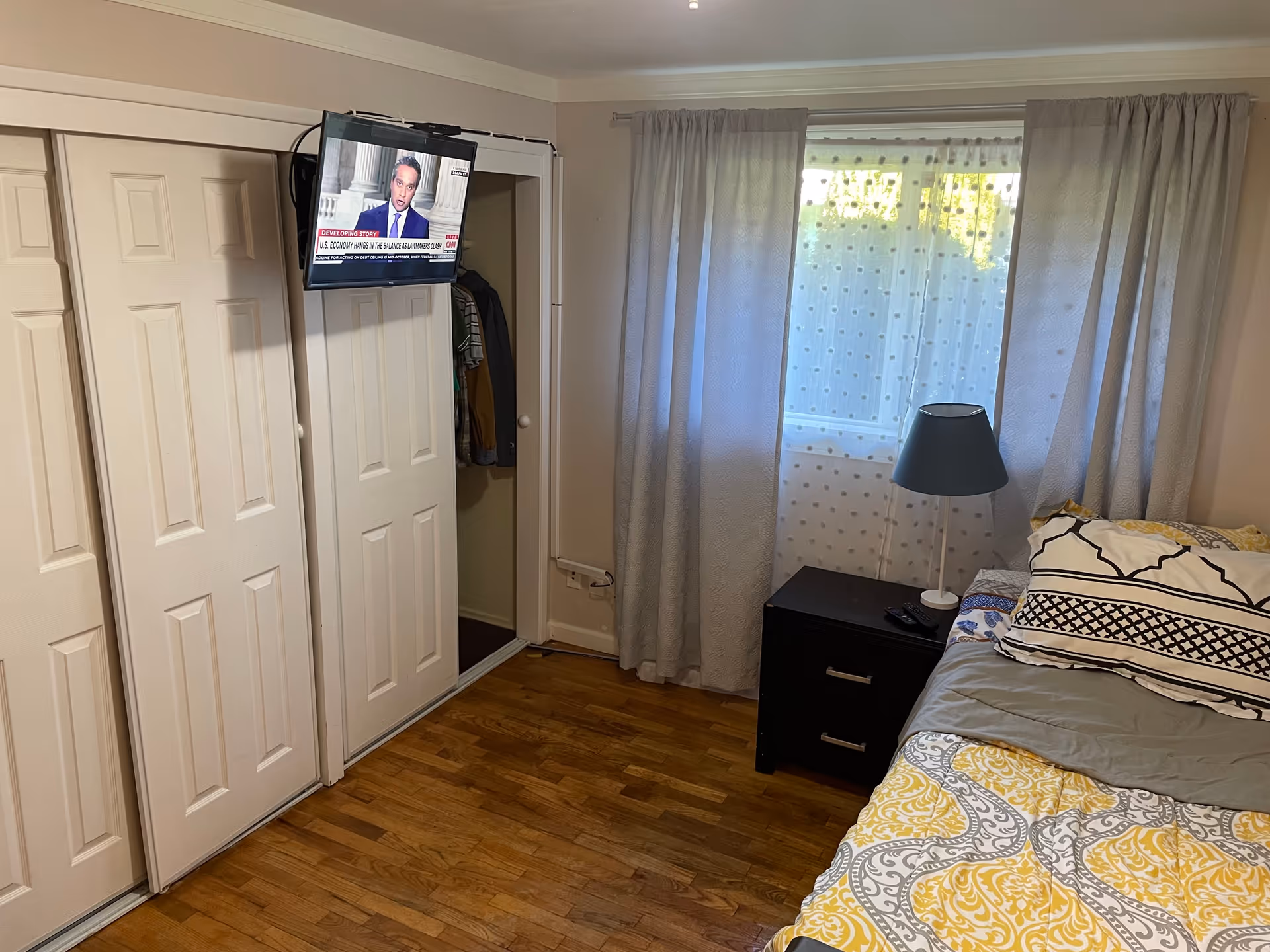Bedroom with bed, nightstand, lamp, window, TV above closet, and sliding white doors.
