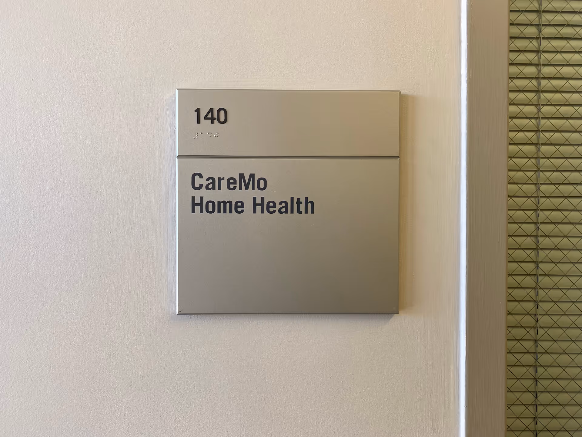 Metal wall sign shows 140 and CareMo Home Health on beige wall