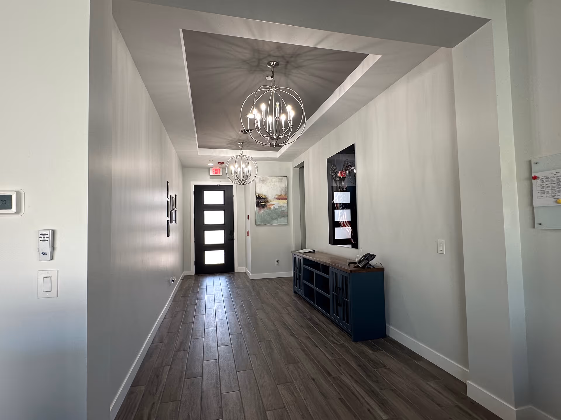 Long, well-lit hallway inside a senior living facility with a dark front door and console table.