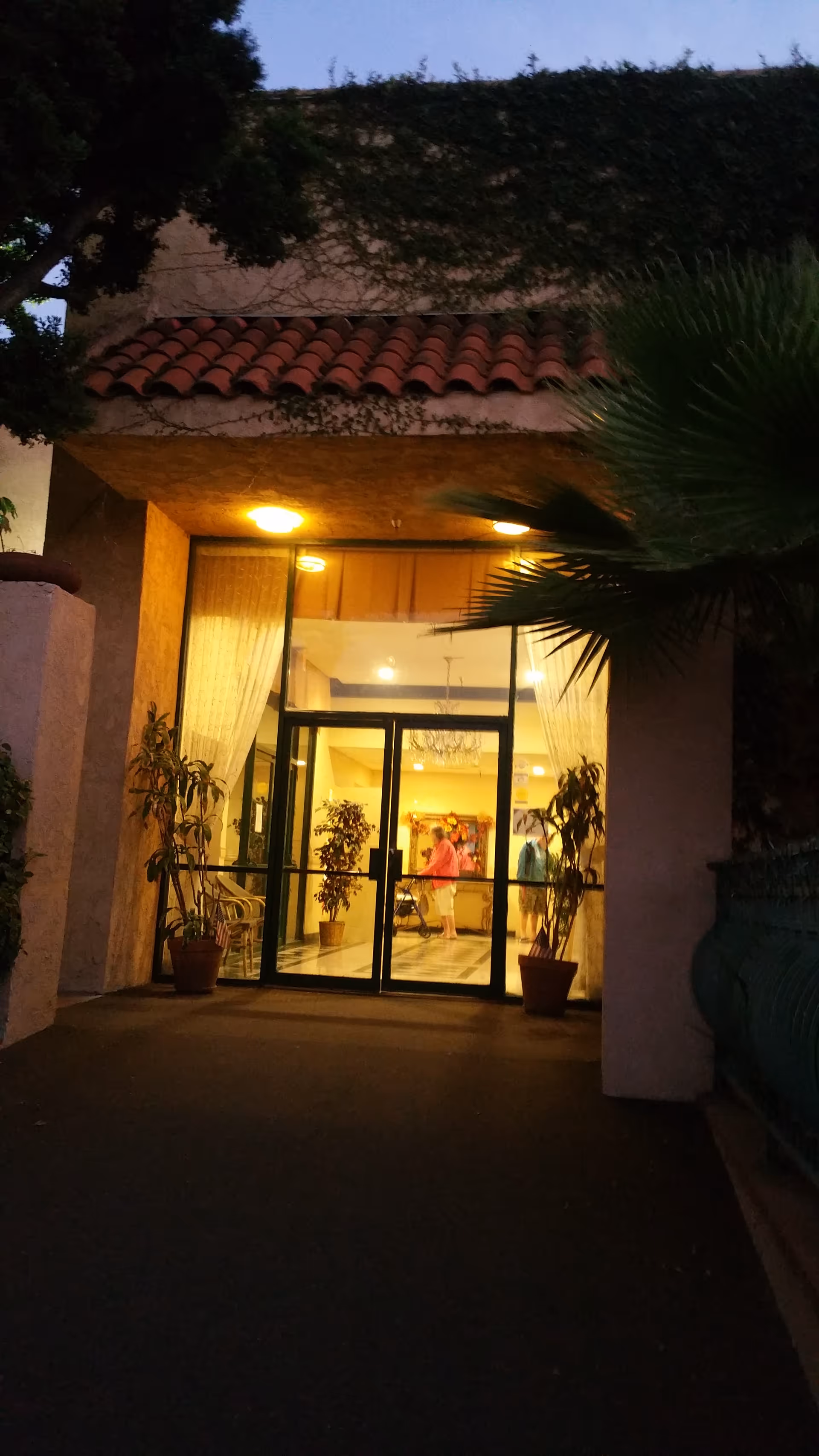 Evening exterior view of Palos Verdes Villa entrance with glass doors and potted plants.