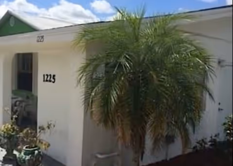 White exterior of a senior living unit with a large palm tree in front.