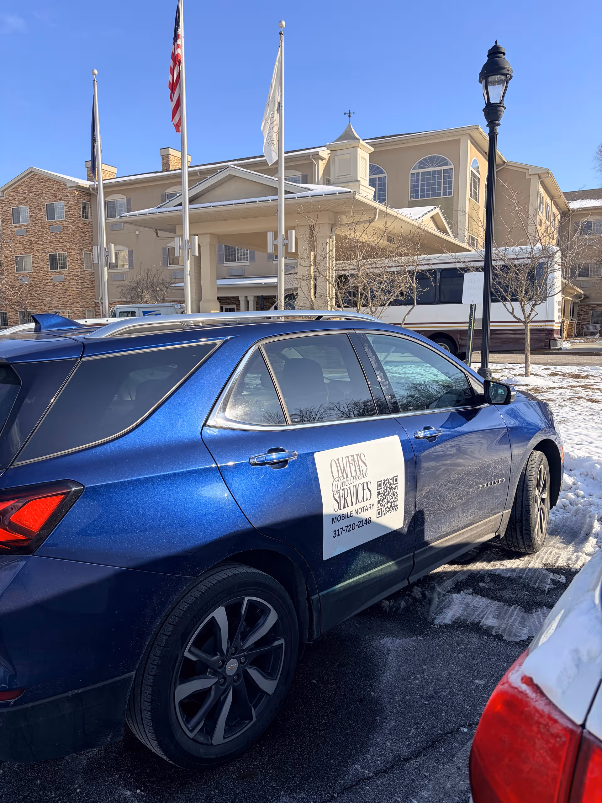 Exterior view of Westside Village Nursing Center with flags, a bus, and a blue car.