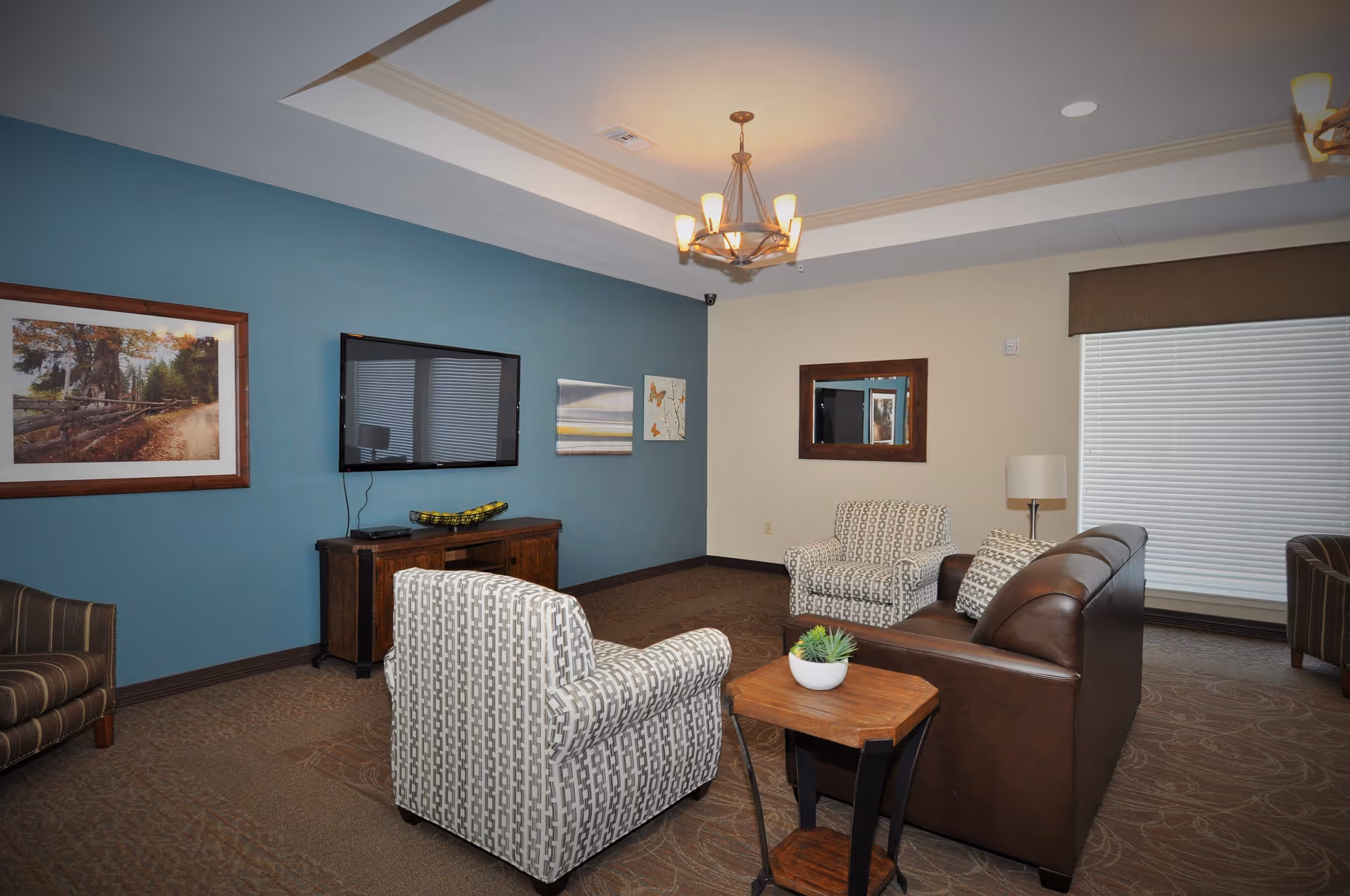 Cozy senior living lounge with blue accent wall, TV, armchairs, sofa, and coffee table.