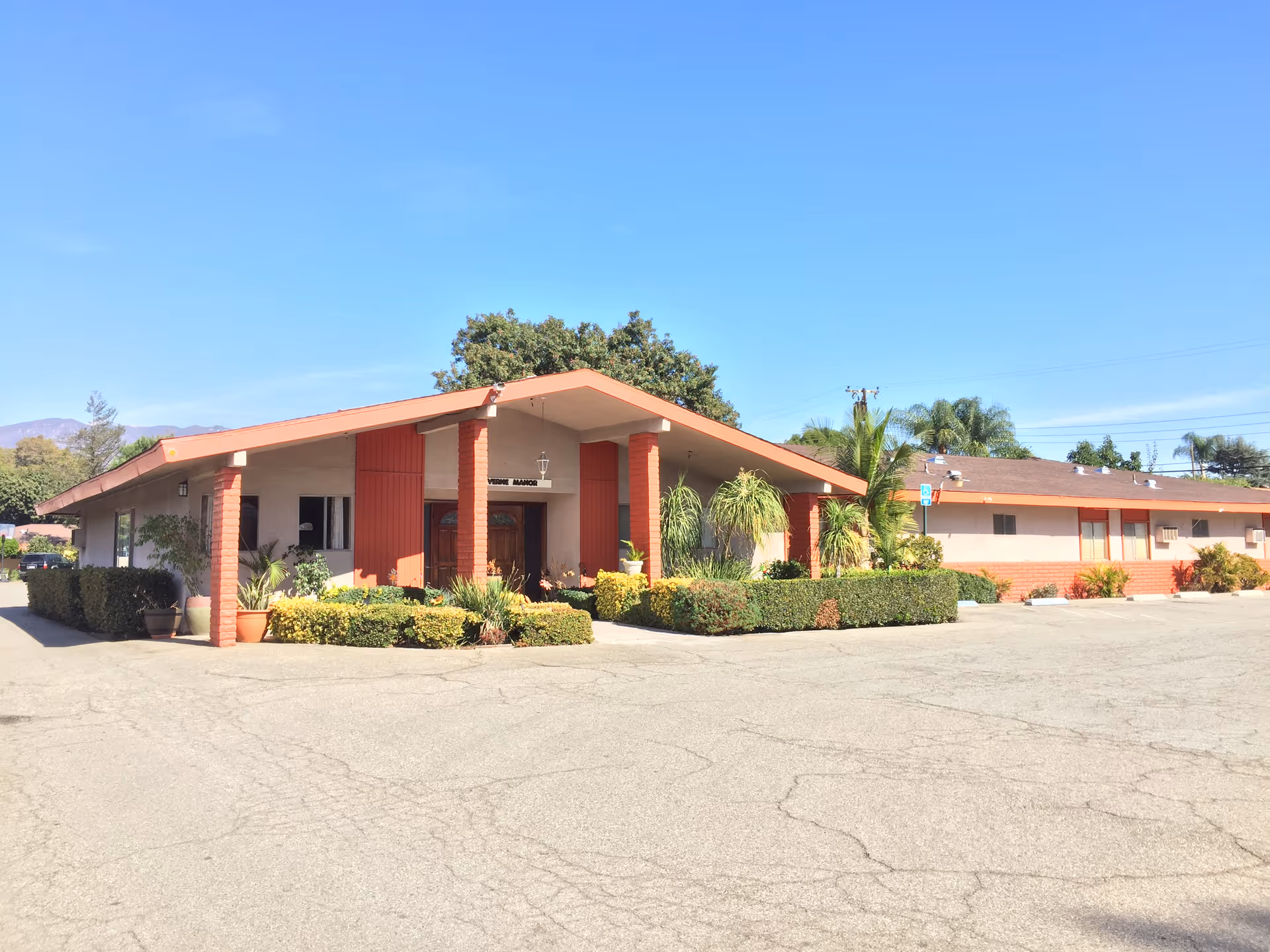 Single-story senior living building with red columns, orange roof, and landscaped entrance.