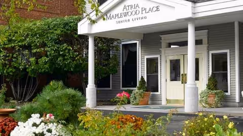 Entrance to Atria Maplewood Place Senior Living with columns, sign, and surrounding greenery.