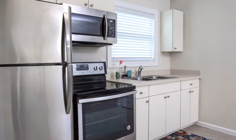 Stainless steel refrigerator, stove, microwave, and white cabinets in a compact kitchen.