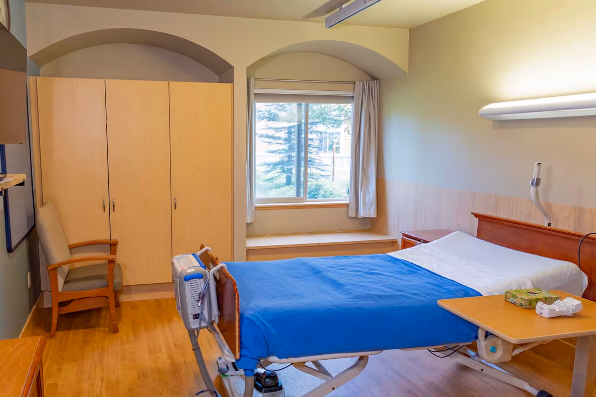 A patient bedroom in a care facility with a bed, wardrobe, and window bench.
