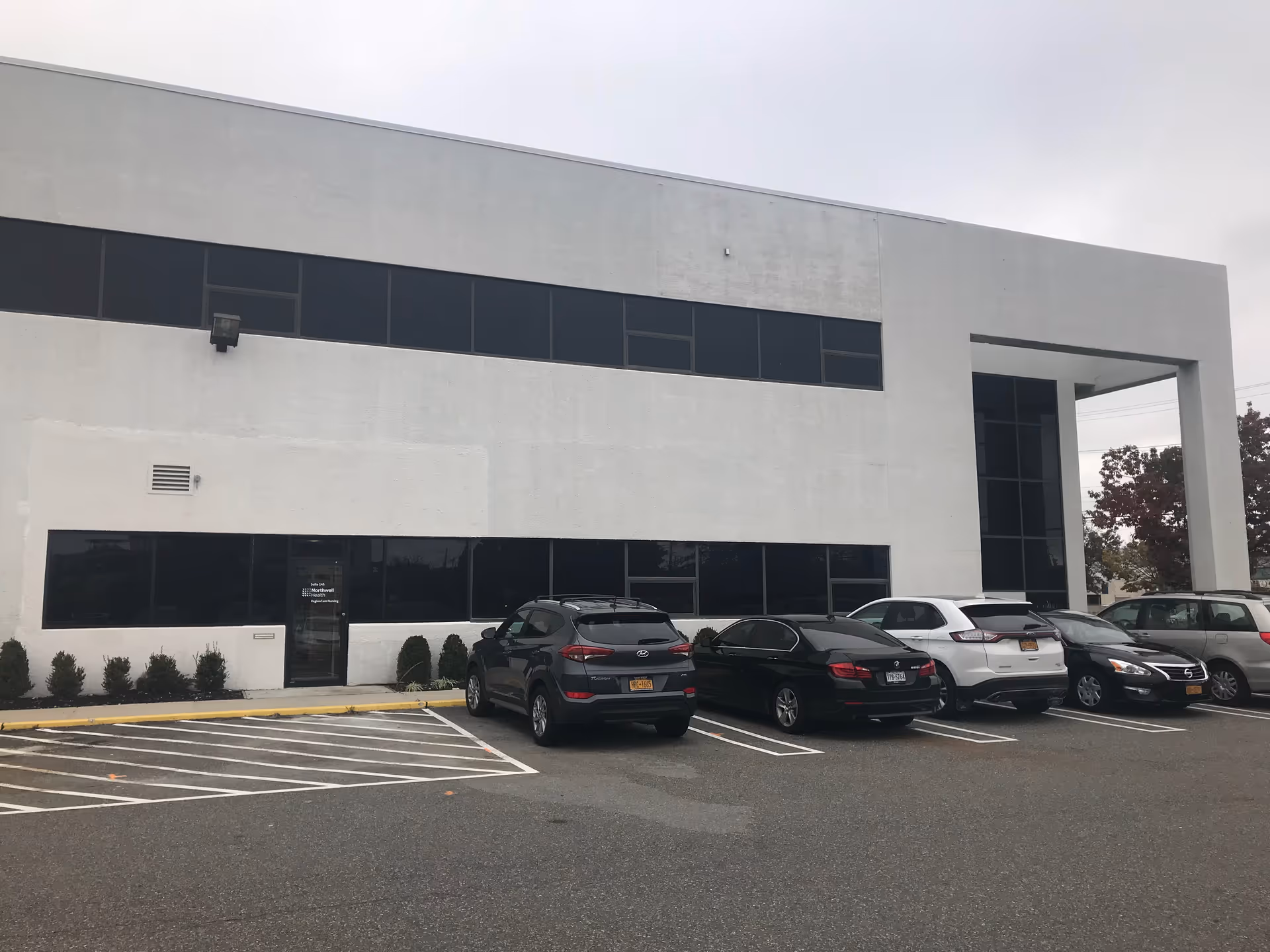 Modern white building with large windows and a parking lot in front.