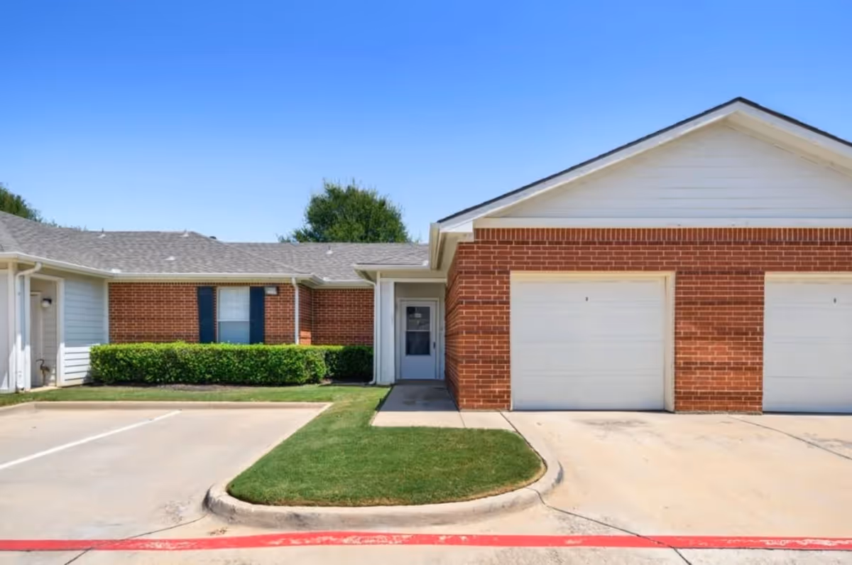 Brick and white senior living facility exterior with attached garages and a manicured lawn.