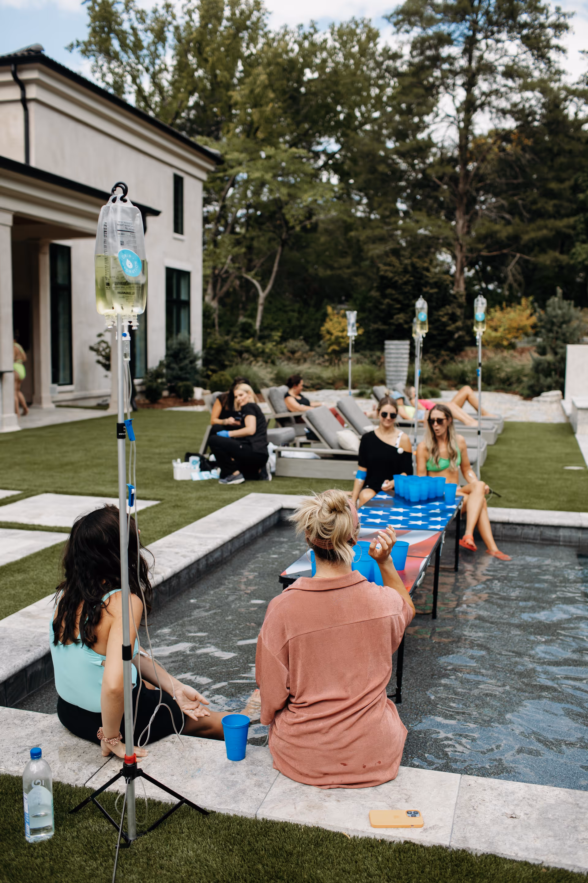 Outdoor poolside area with people seated and IV hydration setup.