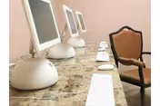 Row of desktop computers with white keyboards on a marble counter in a quiet interior.