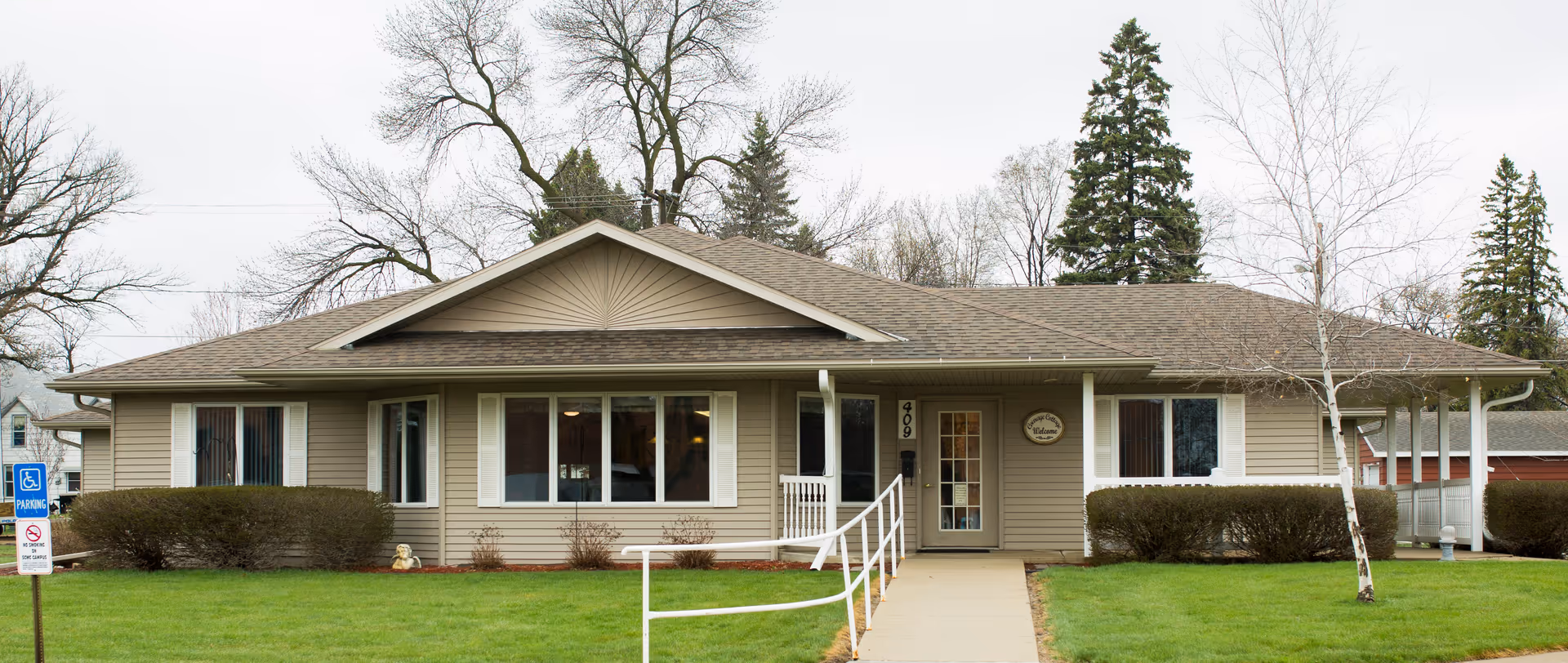 Single-story beige senior living facility exterior with entrance ramp and manicured lawn.