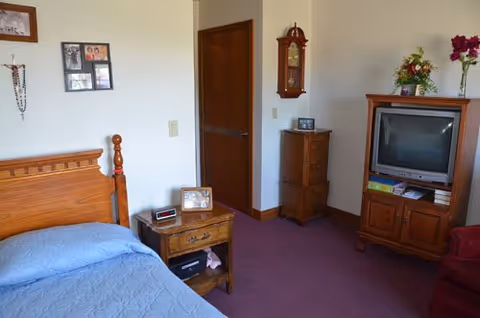 Cozy bedroom featuring wooden furniture, a TV stand, clock, framed photos, and purple carpet.