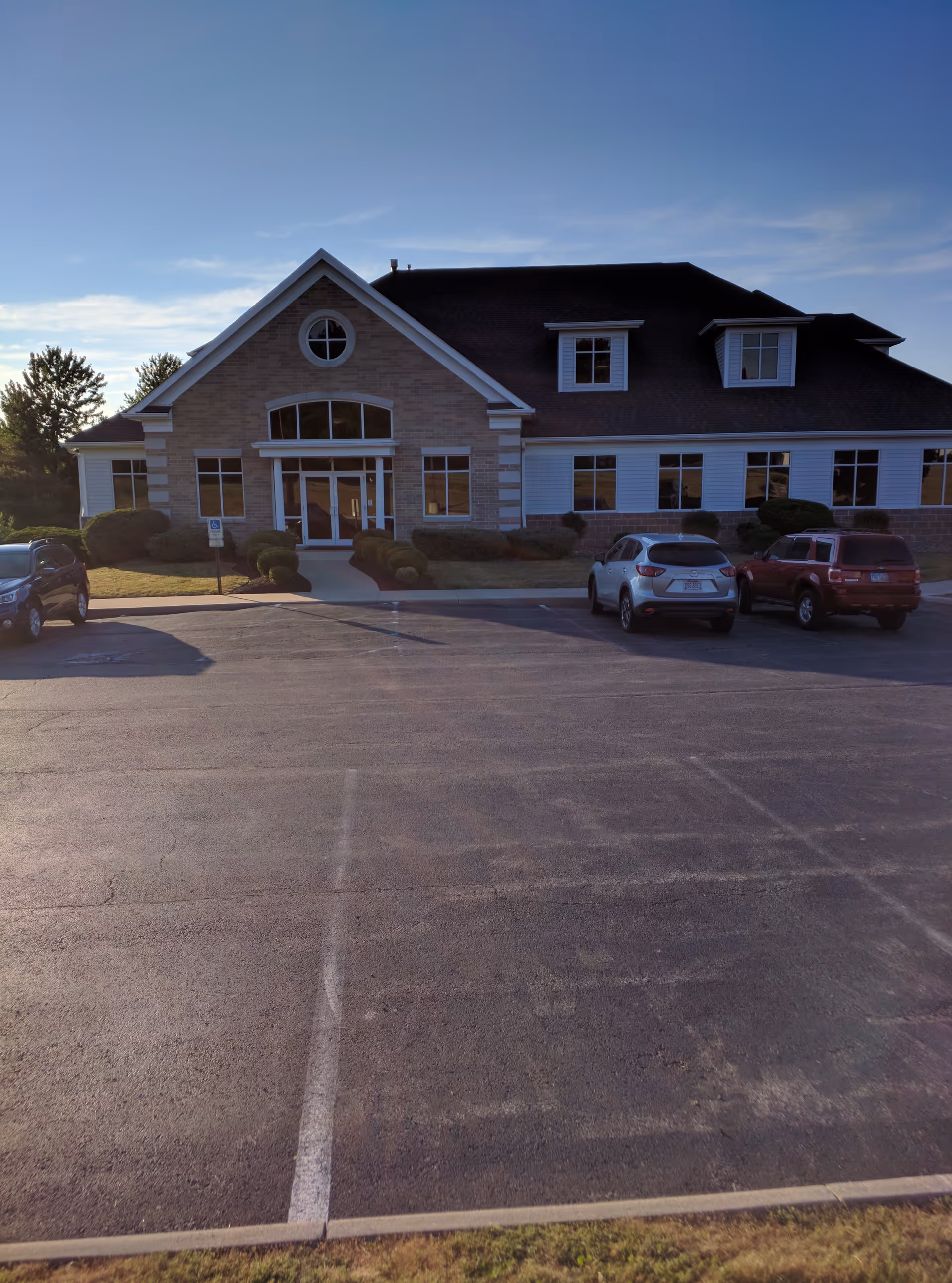 Front exterior view of a brick senior living facility with parked cars and clear sky