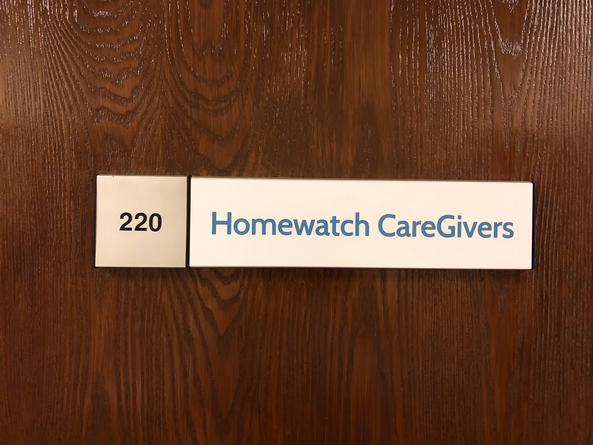 Door sign on a wooden door displaying room number 220 and Homewatch CareGivers.