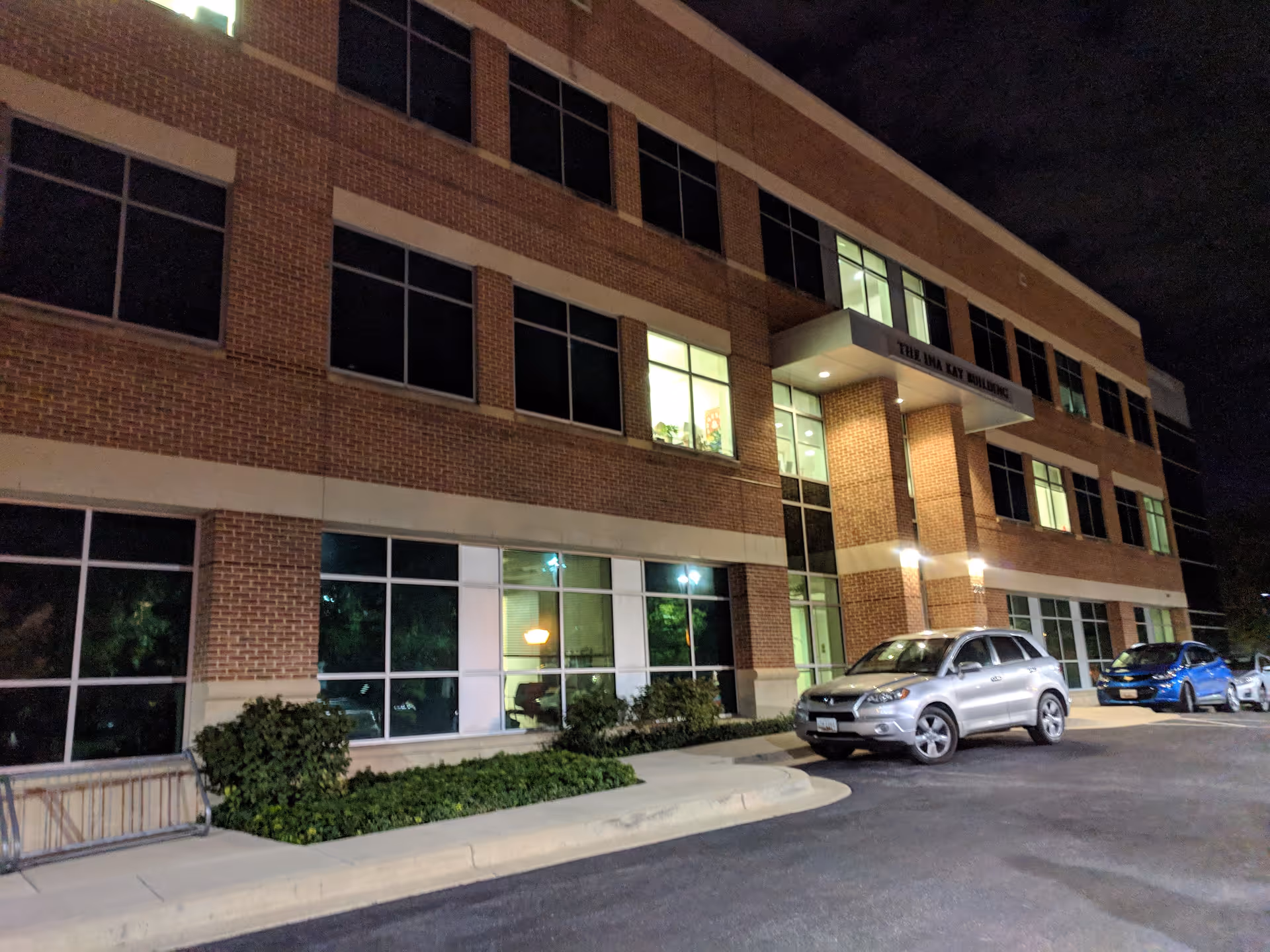 Night-time exterior of a brick senior living building with parked cars and lit entrance.
