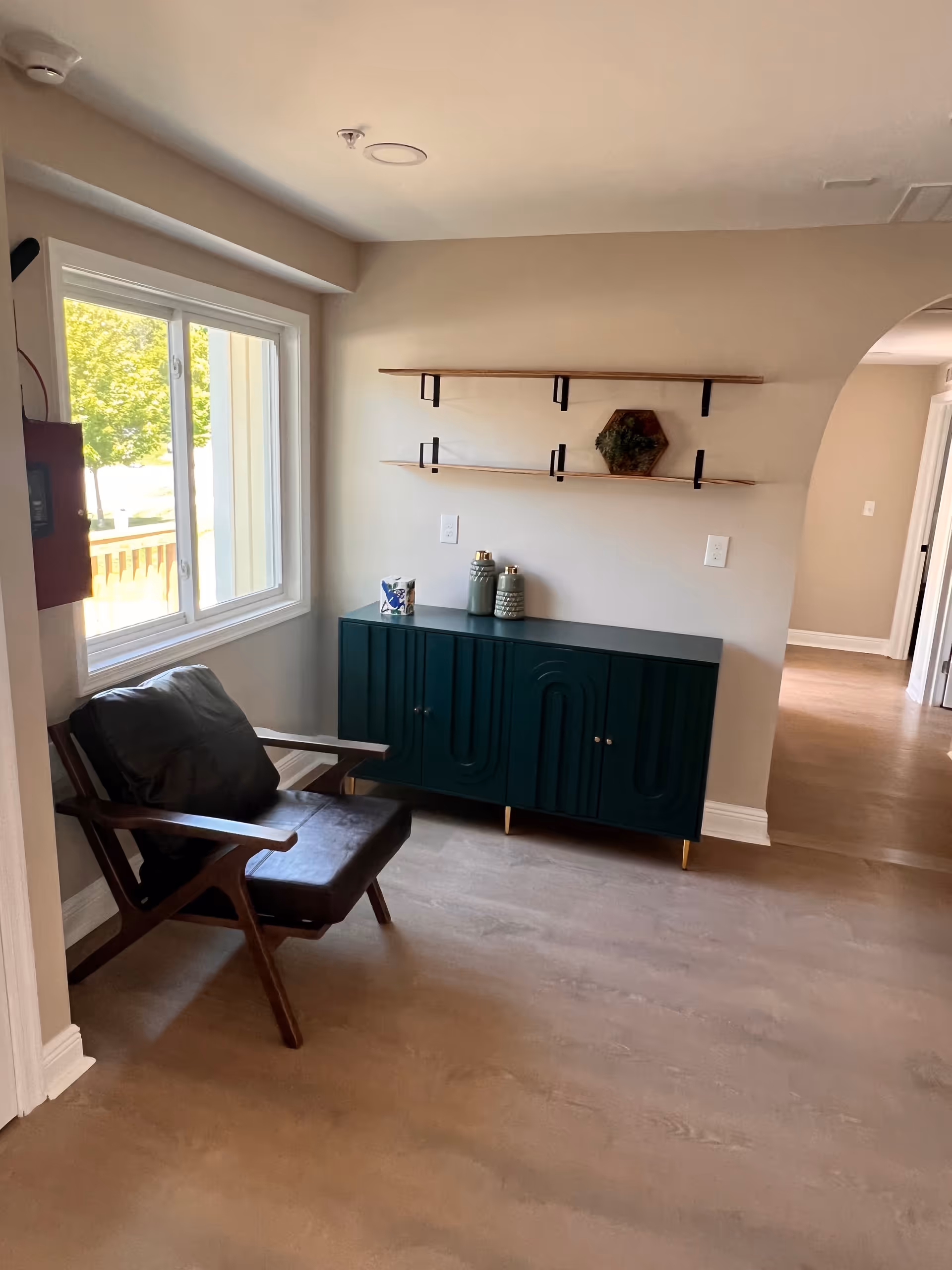 A small living room with a dark green cabinet, two shelves, and a leather chair.
