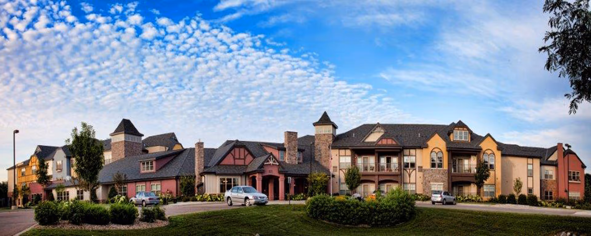A large, multi-wing senior living facility with a manicured lawn and parked cars.
