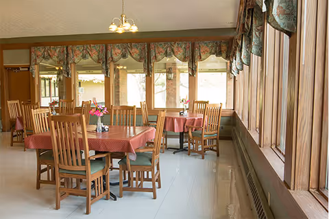 Sunlit dining room with pink tablecloths, wooden chairs, and large windows.