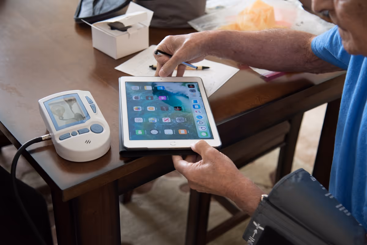 Hands interact with a tablet beside a medical device on a wooden table.