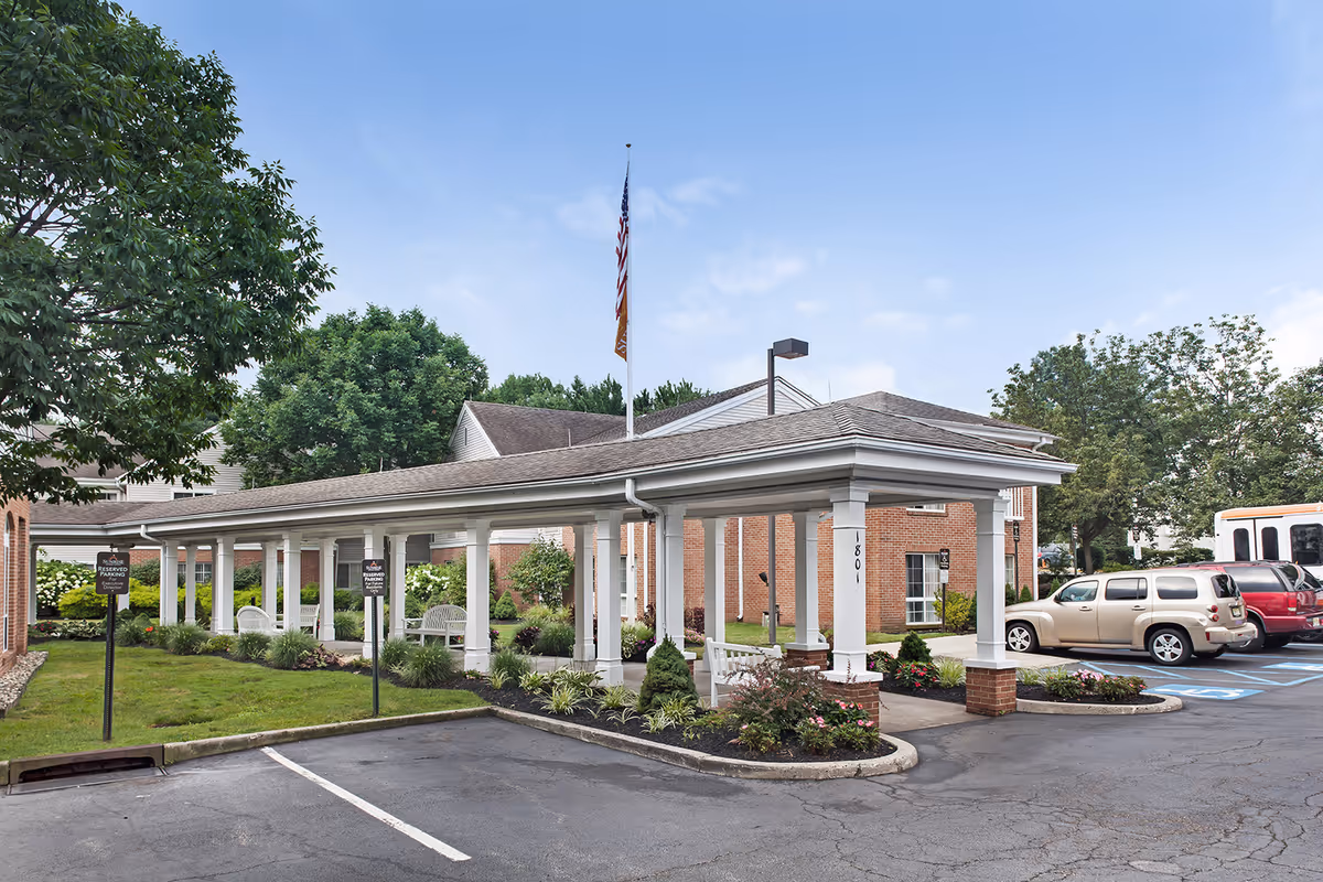 Exterior view of Brighton Gardens of Edison showing a long covered walkway and parked cars.