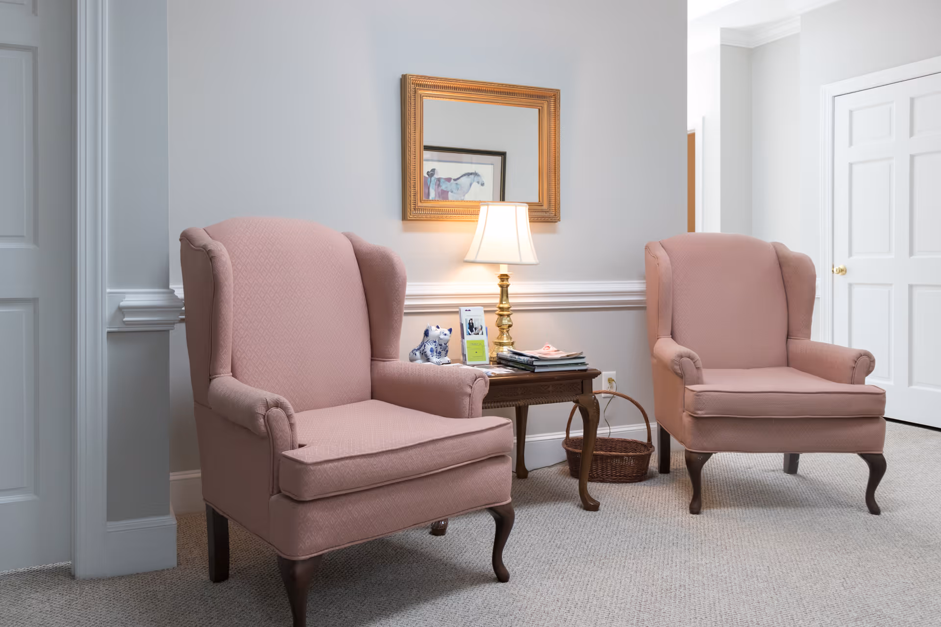 Two pink upholstered armchairs flank a wooden side table with lamp in a cozy living room.