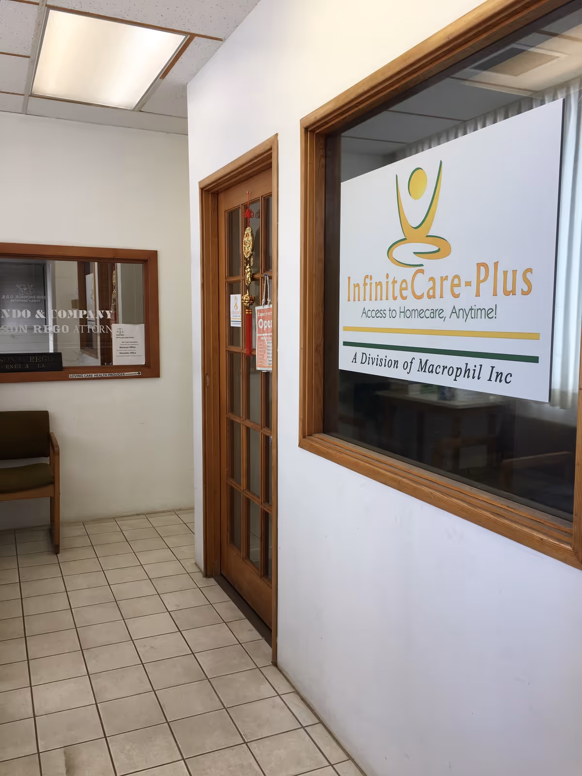 Interior hallway with a glass door, window sign for InfiniteCare-Plus, and tiled floor.