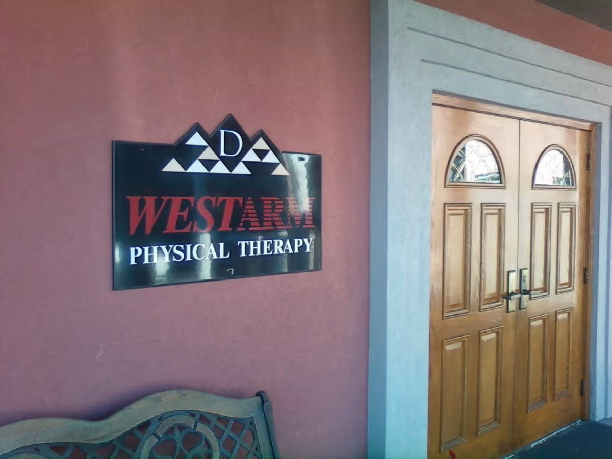 Exterior view of a pink wall with WESTARM Physical Therapy sign and wooden double doors.