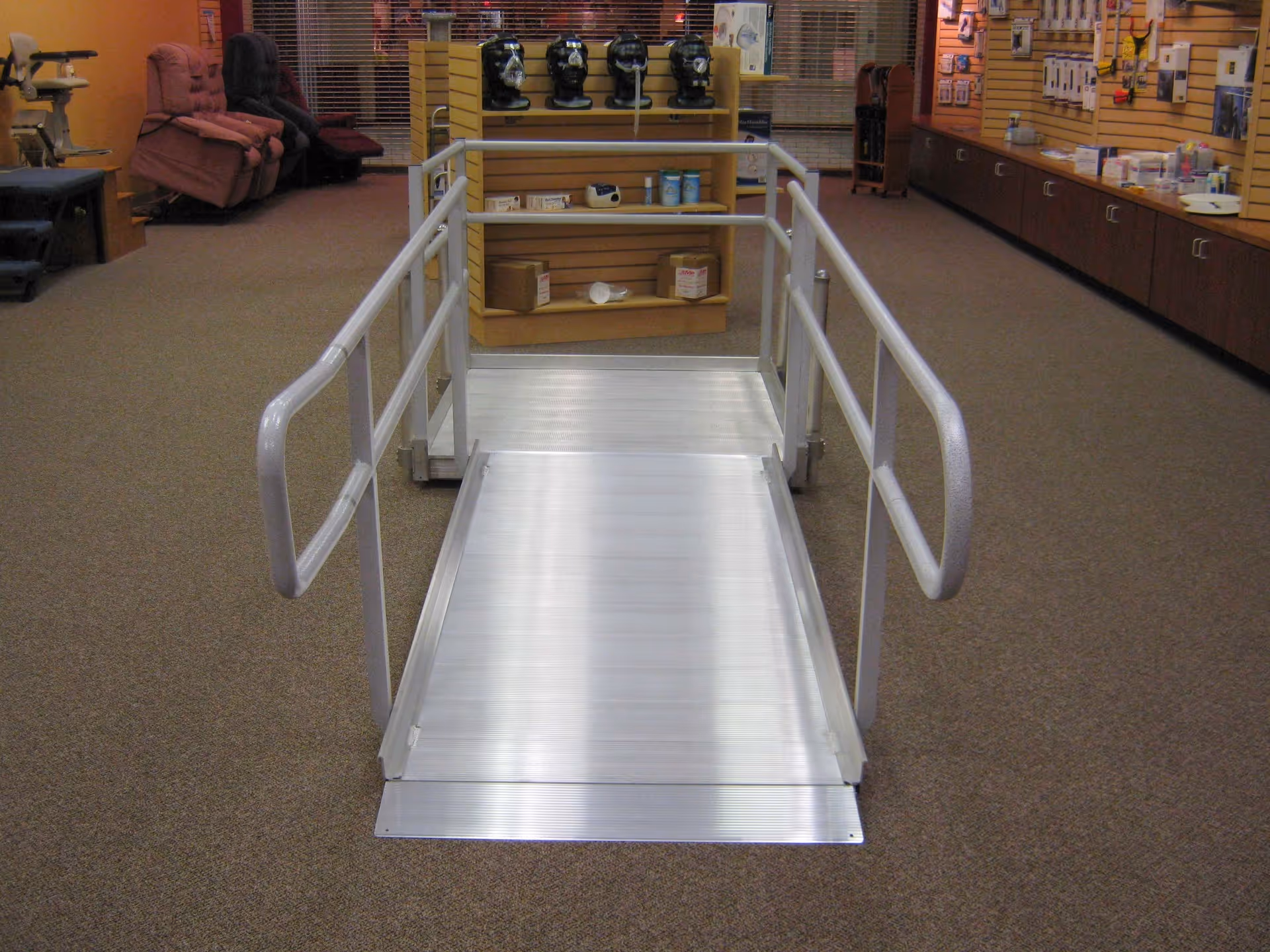 Indoor scene shows a metal wheelchair ramp with handrails in a senior care showroom.
