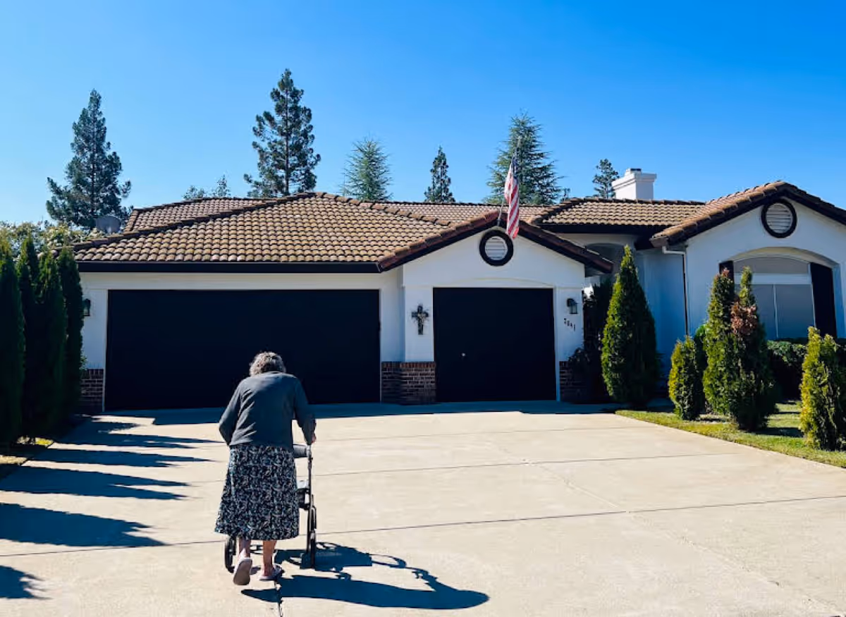 Elderly person with a walker approaches the front of a single-story senior care home.