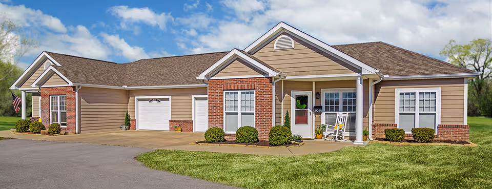 Single-story ranch-style building with a front porch, garage doors, manicured lawn, and shrubs.